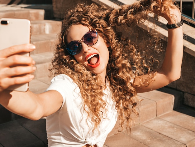 Chica despreocupada sentada en las escaleras en la calle tomando una selfie