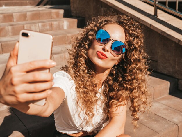 Chica despreocupada sentada en las escaleras en la calle tomando una selfie