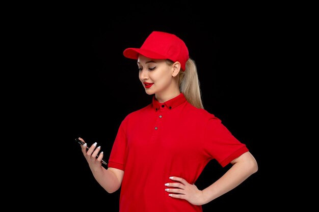 Chica de día de camisa roja mirando su teléfono celular en una gorra roja con camisa y lápiz labial brillante