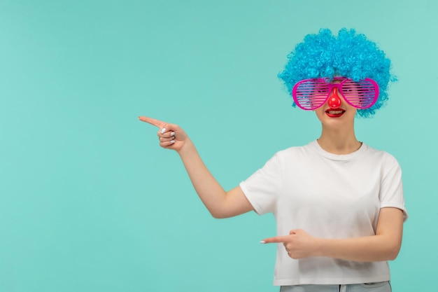 Foto gratuita chica del día de los inocentes sonriendo nariz roja despojada rosa sunglas dedos apuntando payaso cabello divertido