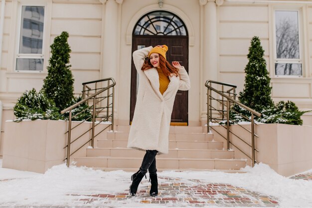 Chica dichosa en bata blanca que expresa emociones positivas en invierno. Tiro al aire libre de hermosa mujer caucásica posando en enero.