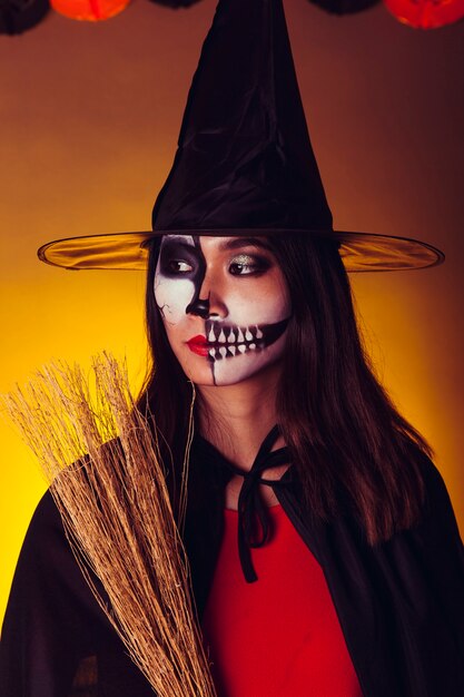 Chica en disfraz de halloween sujetando escoba