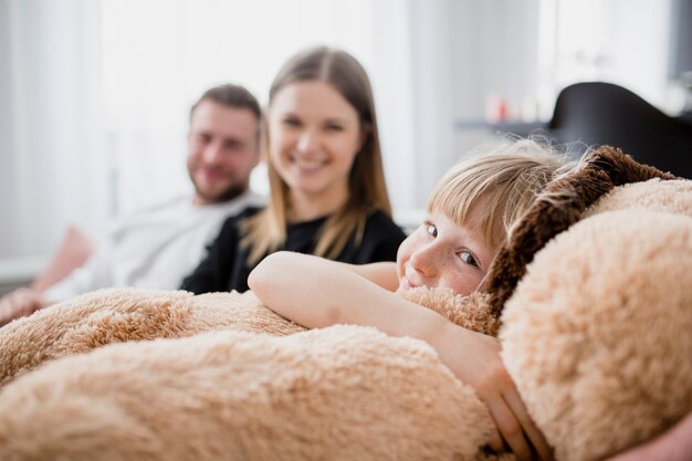 Chica divertida que abraza el juguete cerca de los padres