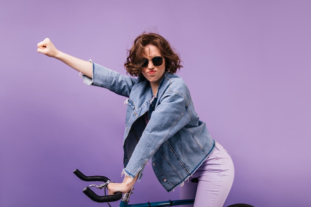 Chica divertida en ropa casual posando en bicicleta. Retrato de dama rizada despreocupada sentada en bicicleta.