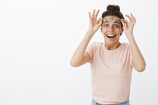 Chica divertida y sorprendida con gafas posando contra la pared blanca