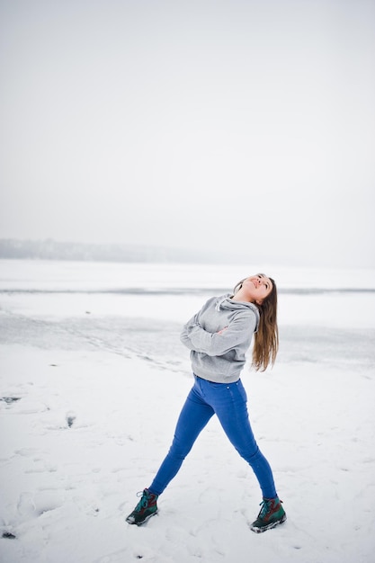 Una chica divertida usa un suéter con capucha y jeans en un lago congelado en un día de invierno
