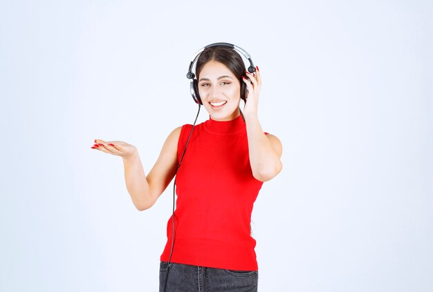 Chica Dj en camisa roja con auriculares apuntando algo o mostrando algo en su mano.