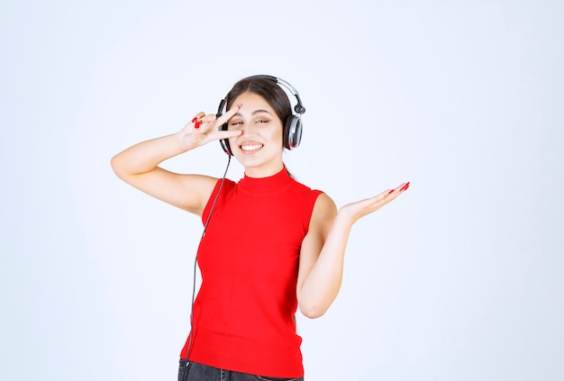 Foto gratuita chica dj en camisa roja con auriculares apuntando algo o mostrando algo en su mano.