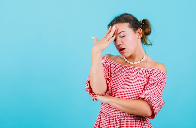 Chica con dolor de cabeza está sosteniendo la mano en la frente sobre fondo azul.