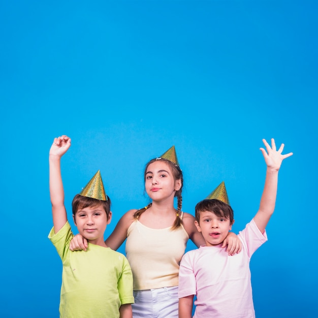 Chica y dos niños con el brazo levantado sobre fondo azul