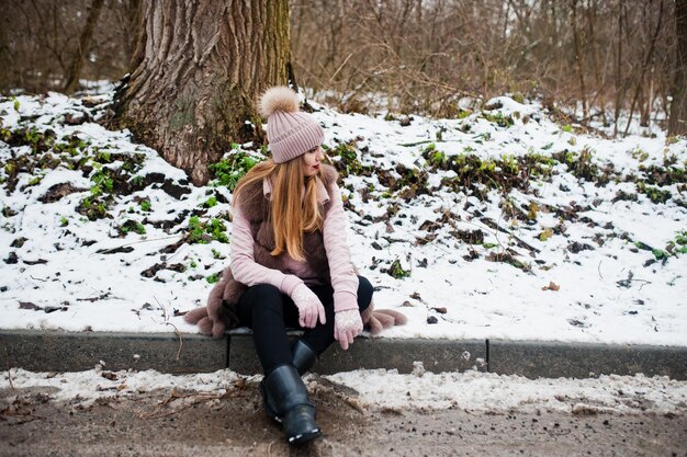 Chica elegante con abrigo de piel y sombreros en el día de invierno en el borde de la carretera