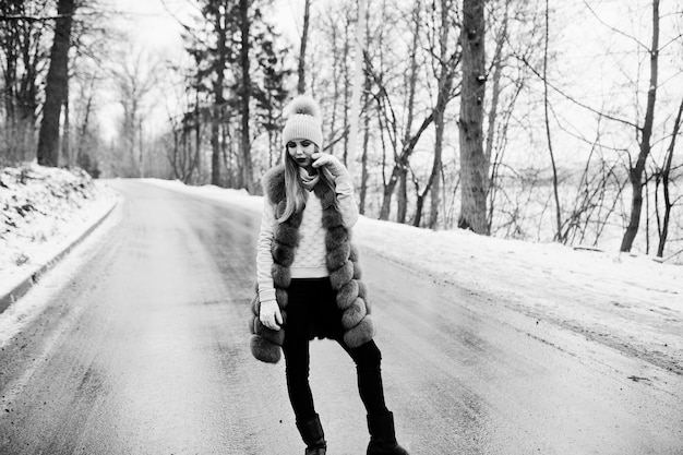 Chica elegante con abrigo de piel y sombreros en el día de invierno en la carretera