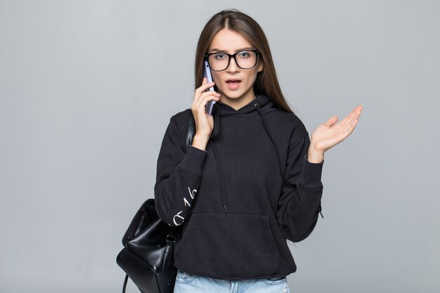 Chica elegante atractiva riendo alegremente mientras habla por teléfono móvil a su novio, aislado en la pared gris.