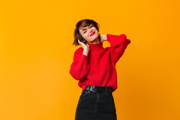 Chica elegante de ensueño tocando el pelo corto Foto de estudio de mujer atractiva sonriente en suéter rojo