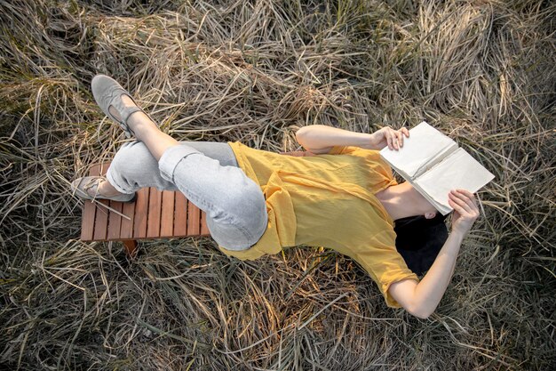 Chica elegante con un libro en sus manos se encuentra entre la hierba en la naturaleza.