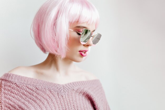 Chica elegante con el pelo corto de color rosa disfrutando de la sesión de fotos de moda en la pared de luz. maravillosa dama blanca con peluca y suéter morado.