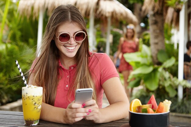 Chica elegante con el pelo largo enviar mensajes a amigos a través de las redes sociales en su teléfono celular