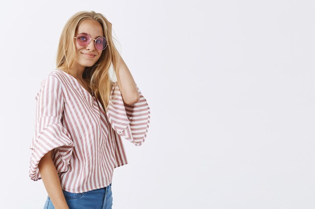 chica elegante posando contra la pared blanca con gafas de sol