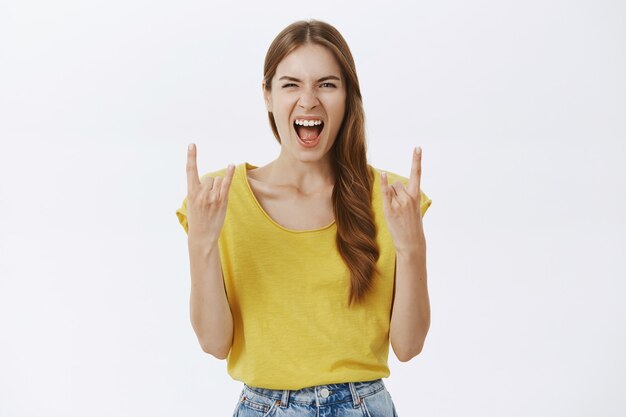 Chica emocionada y alegre divirtiéndose, mostrando gestos de rock-n-roll y disfrutando del concierto