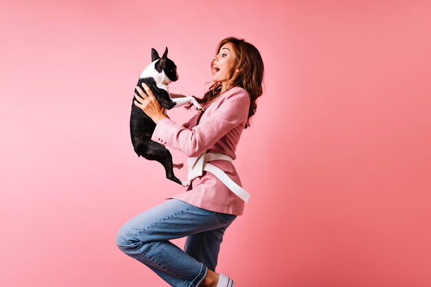 Chica emocionada bailando con bulldog francés. retrato de dama magnífica mirando perro con sonrisa de sorpresa.