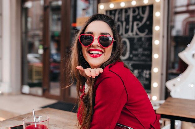 Chica emocionada con cabello castaño claro enviando beso al aire en café