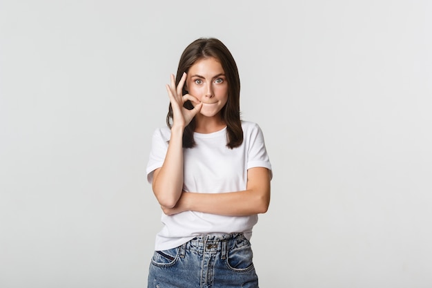 Chica emocionada chismeando, cerrando la boca, manteniendo el secreto.