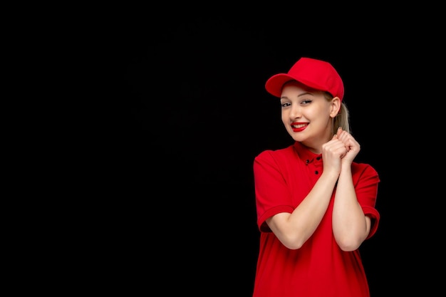 Chica emocionada del día de la camisa roja con las manos en una gorra roja con camisa y lápiz labial brillante