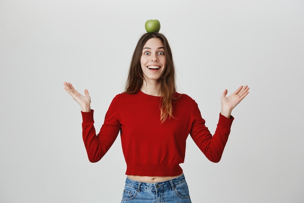 Foto gratuita chica emocionada y divertida sonriendo, sosteniendo la manzana en la cabeza objetivo o objetivo