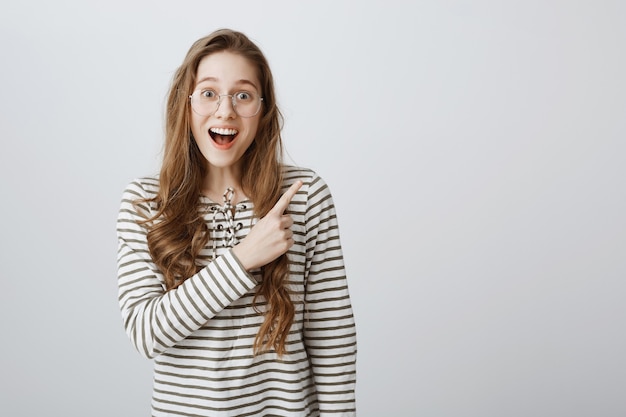 Chica emocionada e impresionada apuntando hacia la esquina superior derecha