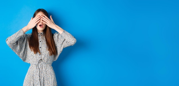 Foto gratuita chica emocionada esperando sorpresa mientras los ojos se cubren con las manos intrigadas en el fondo azul