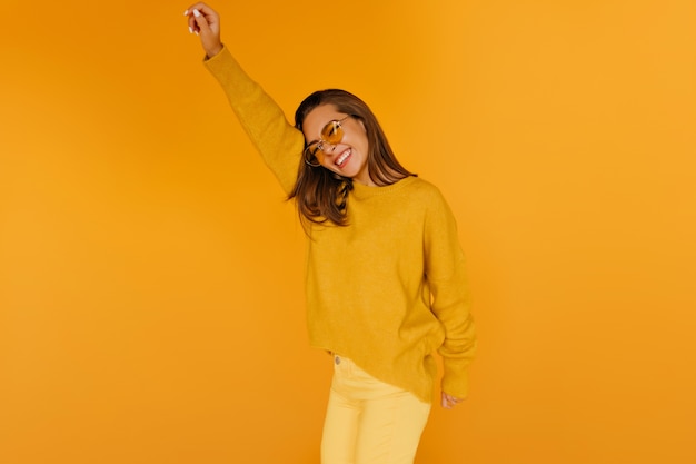 Chica emocionada en pantalones amarillos que expresan emociones sinceras. Señorita guapa con gafas de sol jugando.