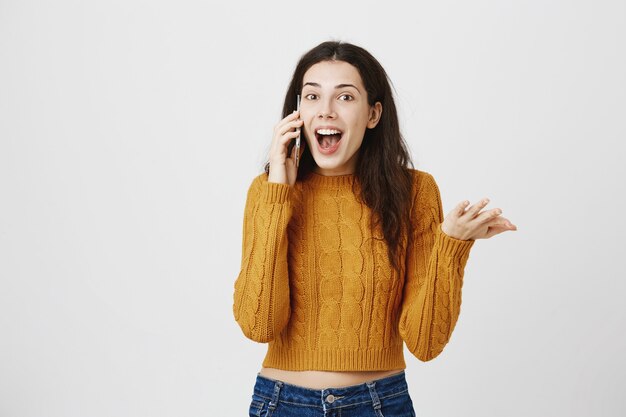 Chica emocionada recibe buenas noticias por llamada telefónica, hablando por teléfono inteligente