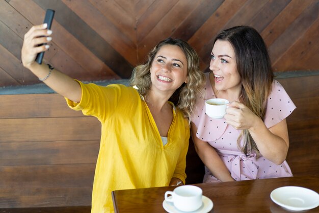 Chica emocionada tomando fotos con su mejor amiga en el café