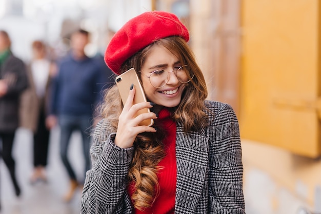 Chica emocional con cabello brillante hablando por teléfono, cruzando la calle