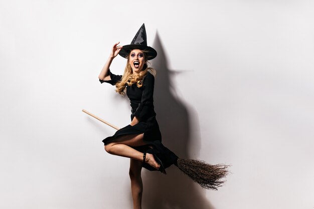 Chica emocional en traje de carnaval expresando felicidad en halloween. encantadora dama rubia lleva sombrero mágico.