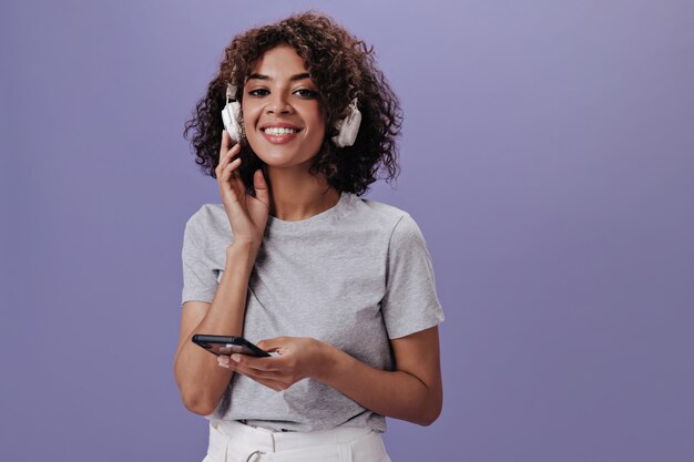 Chica encantadora en camiseta ligera está escuchando música y sosteniendo el teléfono