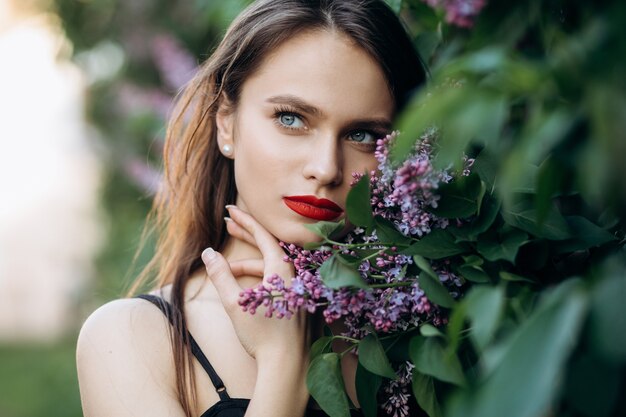 La chica encantadora se encuentra cerca de arbustos con flores