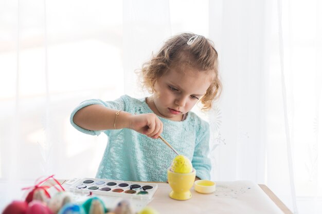 Chica encantadora pintando huevo con amarillo