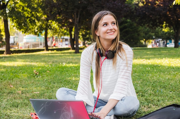 Chica encantadora posando en el parque con la computadora portátil