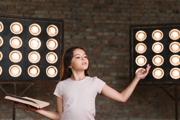 Chica ensayando contra la pared de ladrillo con luz de escenario