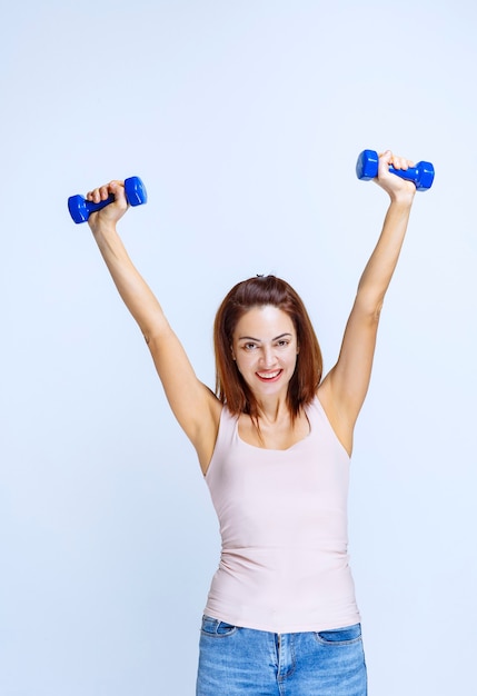 Chica entrenando con mancuernas azules y levantándolas en posición paralela.