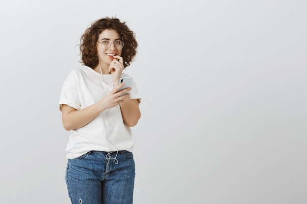 Chica enviando texto arriesgado, mirando emocionado, sonriendo y mordiendo el dedo, sosteniendo el teléfono móvil