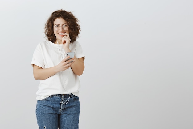 Chica enviando texto arriesgado, mirando emocionado, sonriendo y mordiendo el dedo, sosteniendo el teléfono móvil