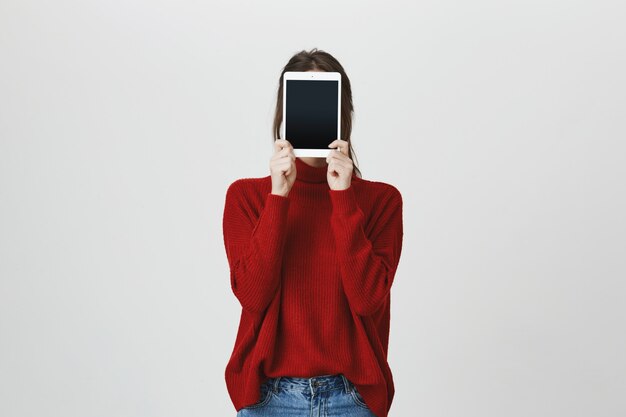 Chica escondiendo la cara detrás de la tableta digital, mostrar pantalla