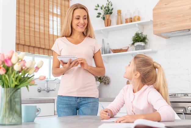 Chica escribiendo tarea supervisada por mamá