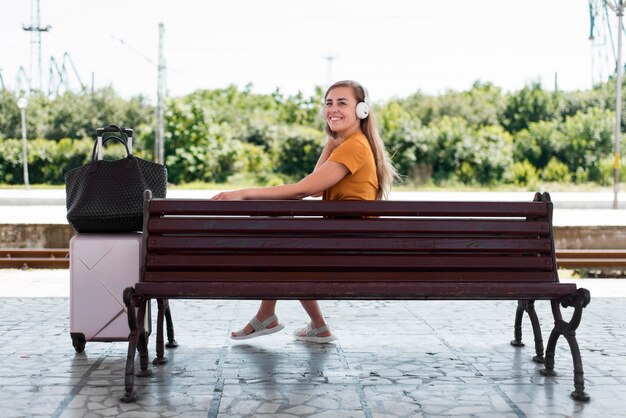 Chica escuchando música en un banco en la estación de tren