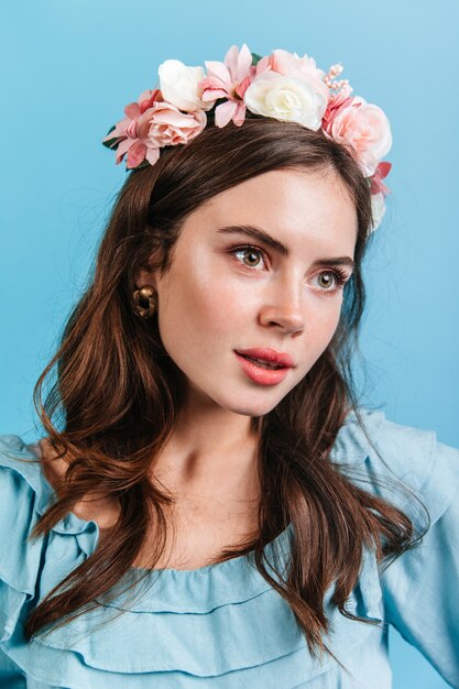 Chica eslava en traje suave mira a la distancia. Retrato de mujer joven con flores rosas en cabello ondulado.