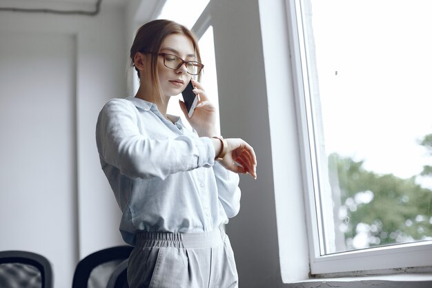 Chica está de pie junto a la ventana. Mujer hablando por teléfono. Morena mira su reloj