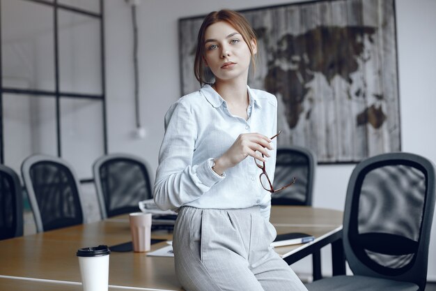 Chica está sentada en la mesa. Mujer sosteniendo vasos en sus manos. Belleza mira a la cámara