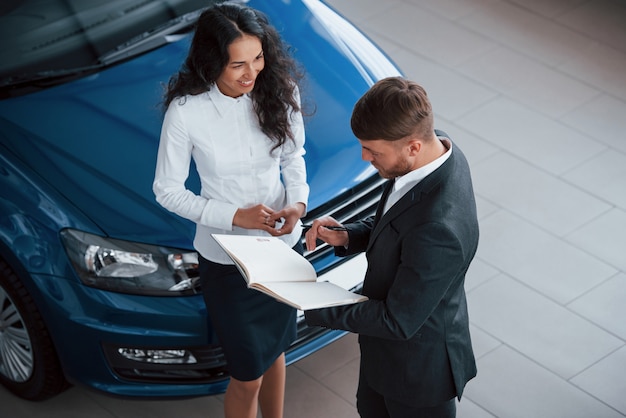 Chica está sonriendo. Clienta y empresario barbudo con estilo moderno en el salón del automóvil